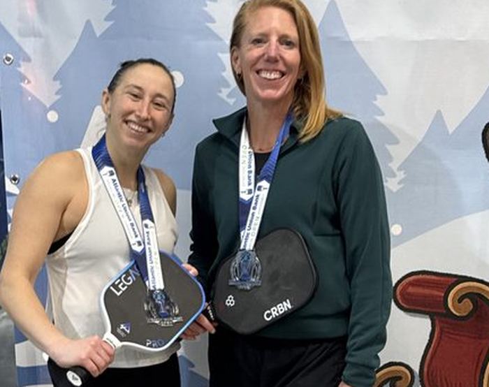 Two pickleball doubles partners on a silver medalist podium with their medals and paddles
